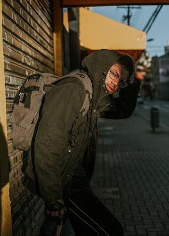 Shallow Focus Photography of Man Carrying Grey Backpack  Leaning on Wall