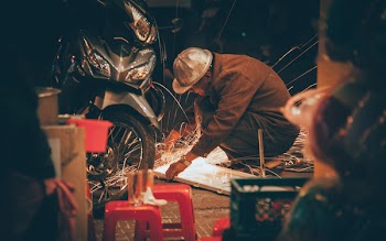 Shallow Focus Photography of Man in Brown Jacket Wearing Gray Hat in Front of Motorcycle