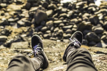 Shallow Focus Photography of Person Wearing Gray Jeans Sitting in Front Rocks