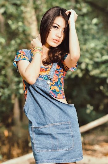 shallow focus photography of woman wearing blue, yellow, and red floral top posing near trees