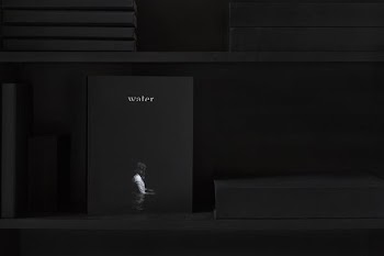 Shelf with books that is dark except for "water" magazine with a person wading on cover