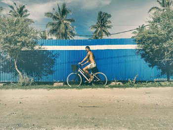 Shirtlless Man Riding On A Bike Near A Fence 