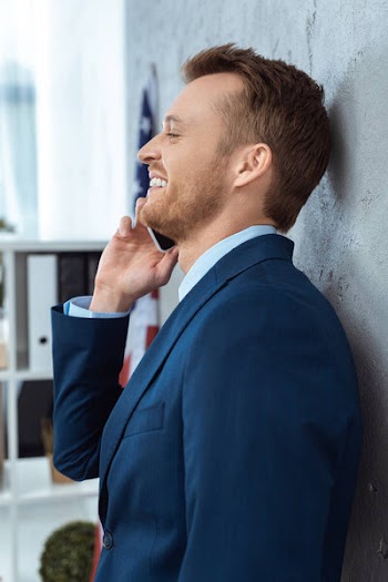 Side view of happy businessman in suit talking on smartphone in modern office