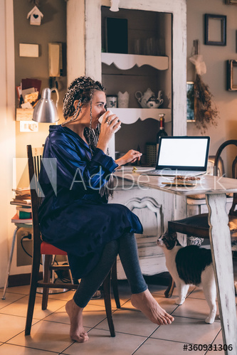 Side view of woman using laptop while drinking coffee at home in morning
