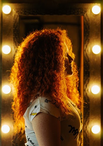 Side View Photo of Girl Standing Near Vanity Mirror