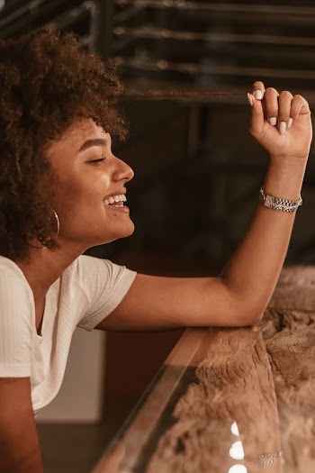 Side View Photo of Laughing Woman in White T-shirt Sitting at the Table While Holding Her Hair