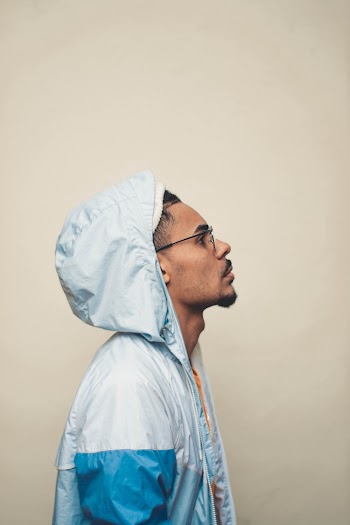 Side View Photo of Man in Glasses and Blue and White Hoodie Posing In Front of Pink Background