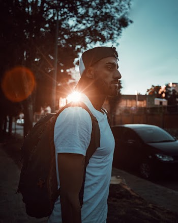 Side View Photo of Man in White T-shirt and Black Backpack Standing on Sidewalk Looking into the Distance