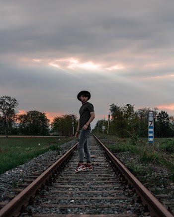 Side View Photo of Man Standing in the Middle of a Train Track Posing