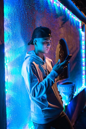 Side View Photo of Man Using Smartphone Leaning on Wall With Colorful Christmas Lights