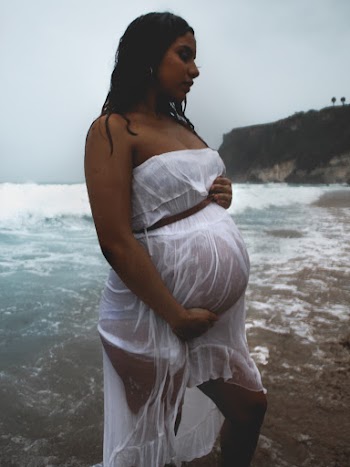 Side View Photo of Pregnant Woman in Wet White Dress Standing on Shore Posing