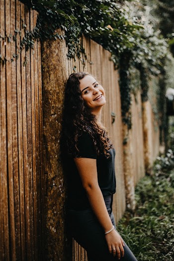 Side View Photo of Smiling Woman in Black T-shirt and Jeans Leaning on Brown Wooden Fence
