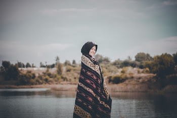 Side View  Photo of Smiling Woman in Hijab Standing by Body of Water While Covering Herself with a Shawl