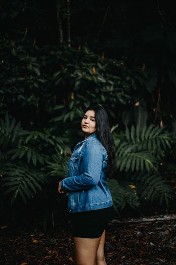 Side View Photo of Woman in  Blue Denim Jacket and Black Shorts Posing Near Green-leafed Plants