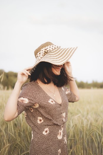 Side View Photo of Woman in Floral Dress and Sun Hat Standing in Grass Field