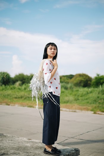 Side View Photo of Woman in White and Red Blouse and Blue Pants Standing on Concrete Surface Posing While Carrying Bag