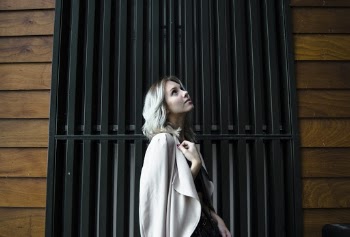 Side View Photo of Woman in White Coat Standing In Front of Black Metal Door Looking Up