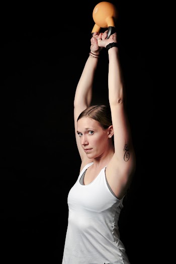 Side View Photo of Woman in White Tank Top Lifting Orange Kettle Bell Standing Against Black Background