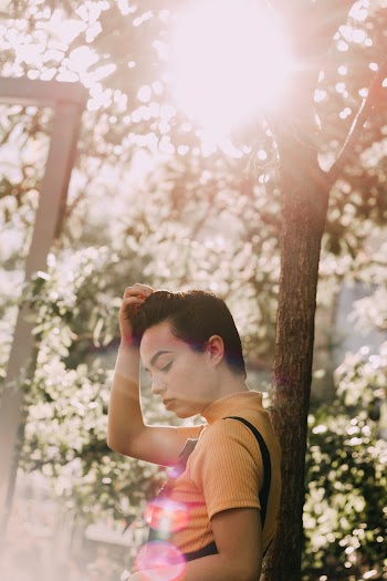 Side View photo of Woman in Yellow Top Leaning on Tree Posing While Looking Down