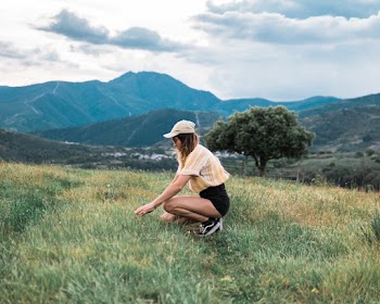 Side View Photo of Woman Kneeling on Grass Field With Mountains in the Background