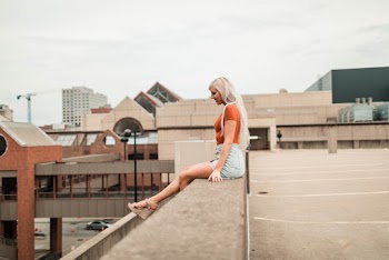 Side View Photo of Woman Sitting on Edge of Brown Concrete Building