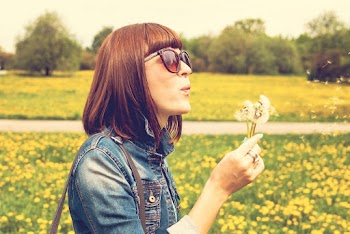 Side View Portrait Photo of Woman in Blue Denim Jacket and Sunglasses Blowing on Dandelion Flowers