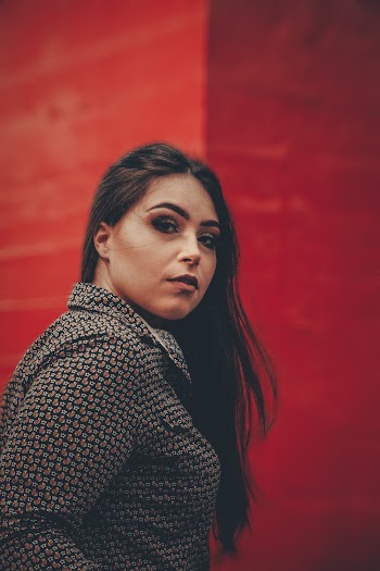 Side View Portrait Photo of Woman Posing Next To Red Building Wall