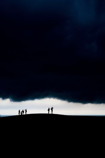 silhouette group of people on hill under dark clouds