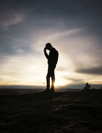 silhouette man standing holding cap during sunset