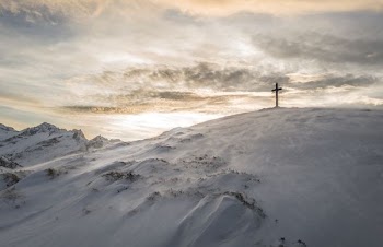 silhouette of brown cross on mountain covered with snow under white clouds