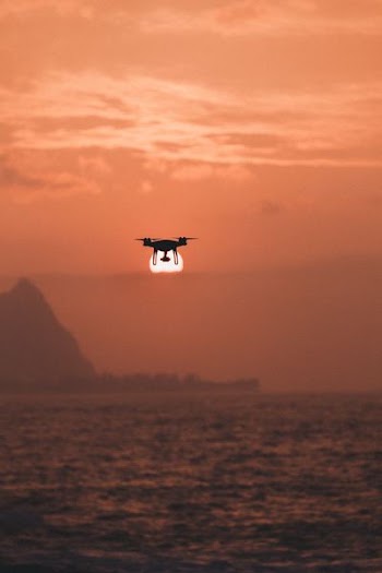 silhouette of drone hovering above body of water