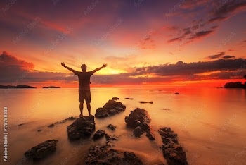 silhouette of happy man standing on rock in the sea with sunset sky, long speed exposure,Tarn-khu beach at Trat, Thailand