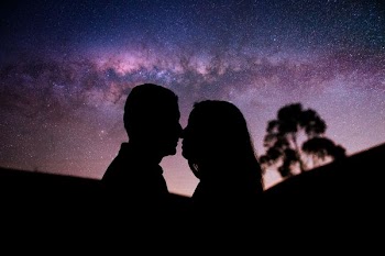 silhouette of man and woman facing each other with milky way background