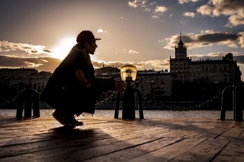 Silhouette of Man Squatting Near Body of Water during Sunset.