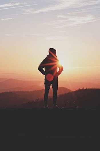 silhouette of man standing near cliff in golden hour background