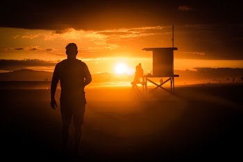 silhouette of man standing near wooden shed during sunset