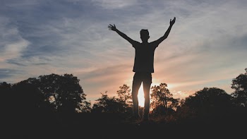 Silhouette of Man Standing on Grass Field Under Blue Sky