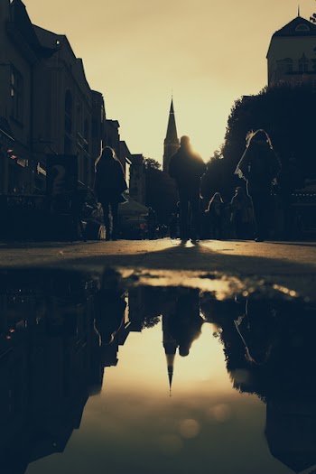 Silhouette of People Walking on Street Reflected on Puddle