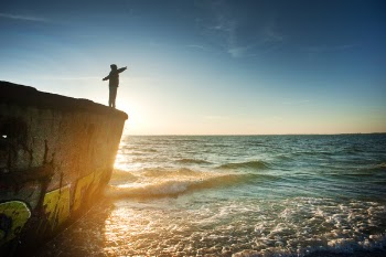 Silhouette of Person on Cliff Beside Body of Water during Golden Hour