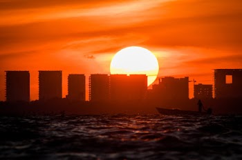 Silhouette of Person Riding Canoe Near Buildings during Sunset