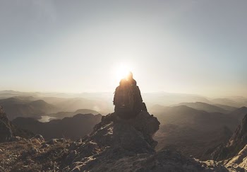 silhouette of person sitting on rock facing mountain range