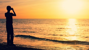 Silhouette Of Person Standing On Seashore During Sunset