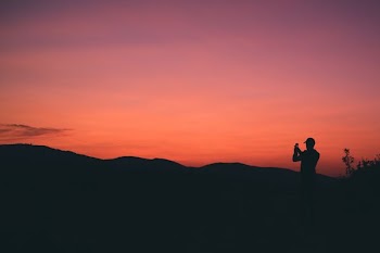 silhouette of person taking photo of mountain during sunset