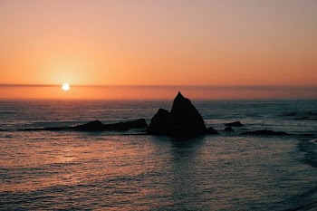 silhouette of rock formation surrounded by body of water at sunset