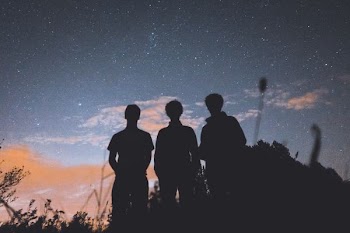 silhouette of three people standing on tall grass during nighttime