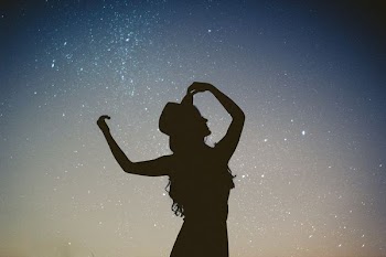 silhouette of woman holding hat in blue and gray nebula