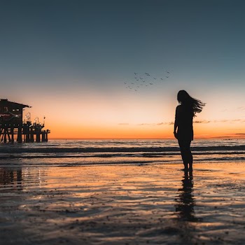silhouette of woman standing at the seashore with crashing waves during golden hour