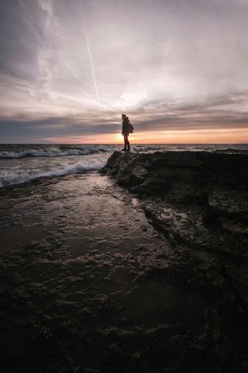 silhouette of woman standing on boulder near seashore during golden hour background