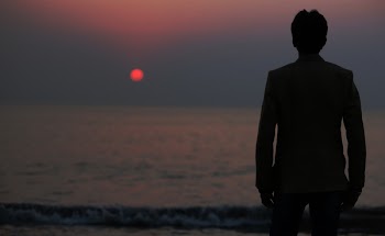 Silhouette Photo of a Man Standing in Front of the Body of Water during Sunset
