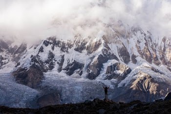 silhouette photo of a person raising hands on top of mountain near gray mountain covered with snow